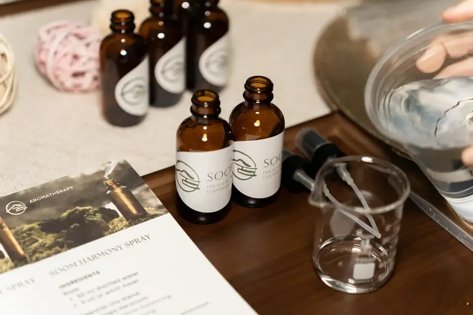 Bottles of aromatherapy oil, a mixing beaker, and a sprayer on a wooden table, with aromatherapy instructions.
