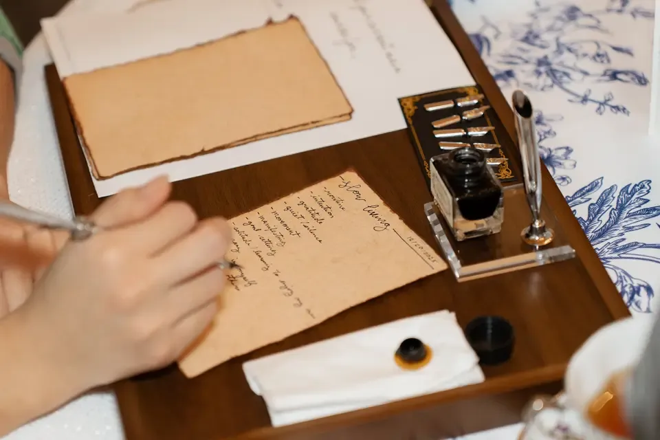 Handwriting on aged paper list of herbs and spices, ink bottle, inkwell, and pen on wooden desk.
