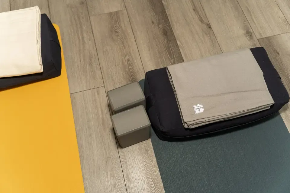 Yoga mat, bolsters, and towel arranged on wooden floor in yoga studio.