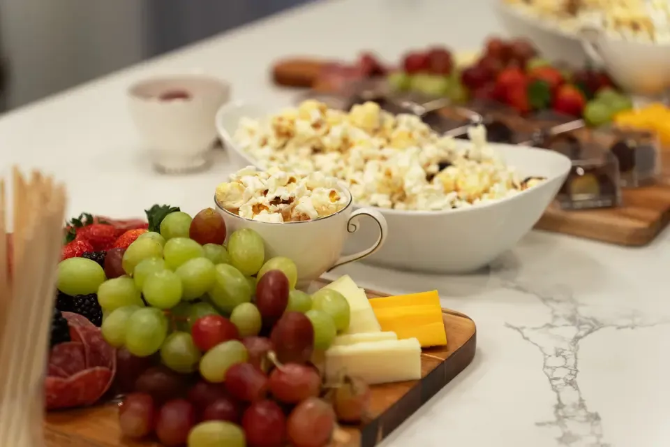 Assorted fresh fruit, cheese, popcorn, and snacks on a buffet table.